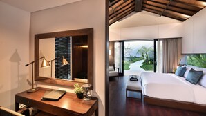 Habitación de hotel con una cama grande, un escritorio con una computadora portátil, un espejo y vistas a un paisaje tropical por la ventana.