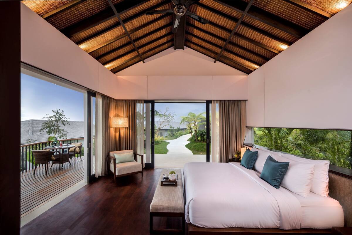 A spacious bedroom with a large bed, a view of a garden, and a balcony with outdoor seating.