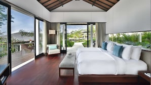 A spacious bedroom with a large bed, a sofa, a coffee table, and a view of a lush garden and pool. - Altavista Villa (Wanagiri)
