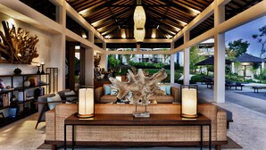 Un espacio interior amplio con techo alto, una zona de estar central con una gran escultura de madera natural, y vistas al jardín exterior.