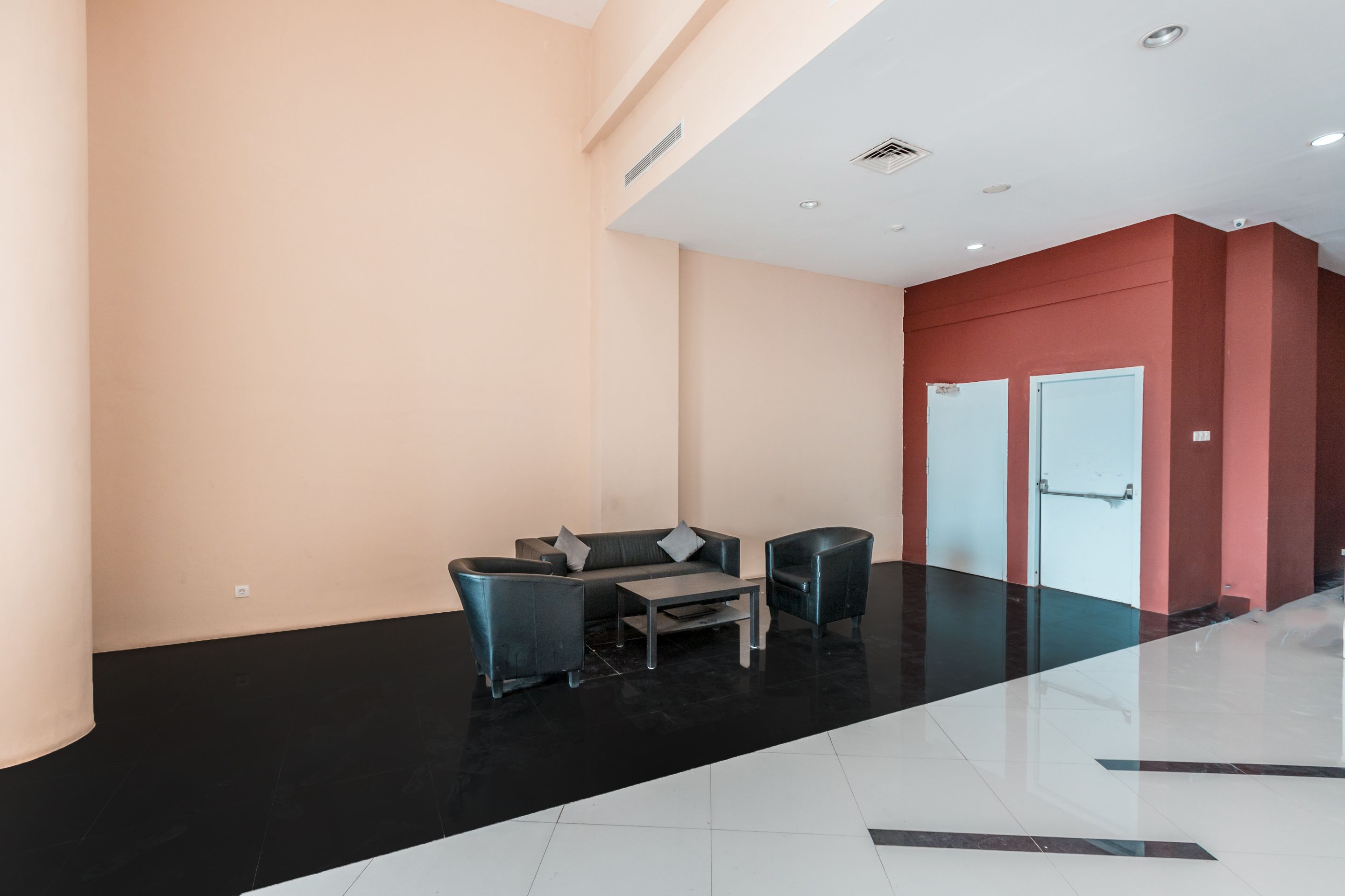 Un lobby moderno con piso de baldosas blanco y negro, un sofá gris, dos sillones y una pequeña mesa de centro.