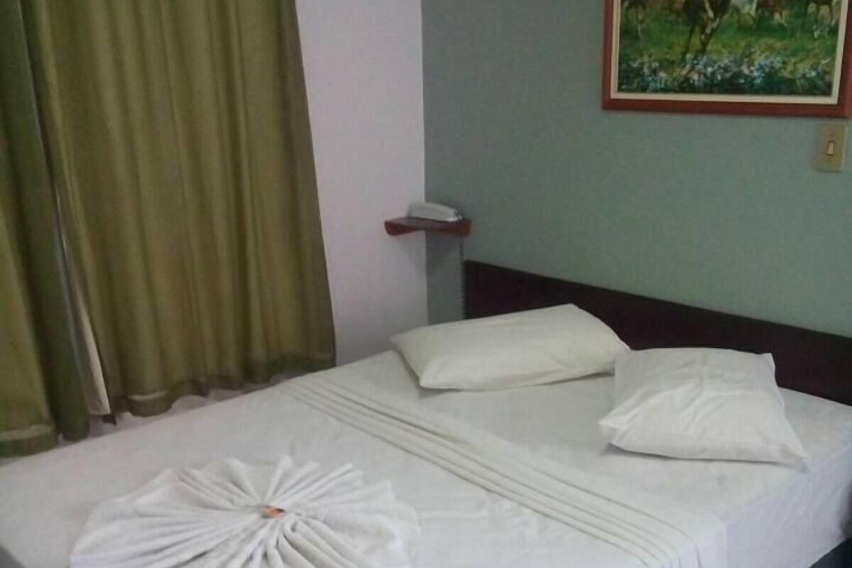 Ein Hotelzimmer mit einem ordentlich bezogenen Bett, einem Bild an der Wand und einem Telefon auf dem Nachttisch.