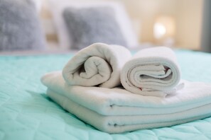 A stack of neatly folded white towels on a teal bedspread.