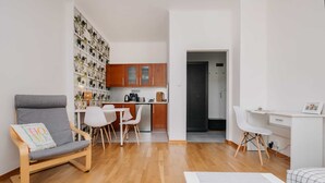 Un ambiente compatto con un divano grigio, un tavolo da pranzo con sedie, un angolo cottura e una scrivania bianca.