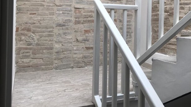 Eine Treppe mit weißen Geländern führt zu einem Raum mit einer Ziegelwand.