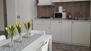 Eine moderne Küche mit weißen Schränken, einem Gasherd, einer Mikrowelle und einem Spülbecken. Ein Esstisch mit Stühlen und eine Vase mit Blumen sind ebenfalls vorhanden.