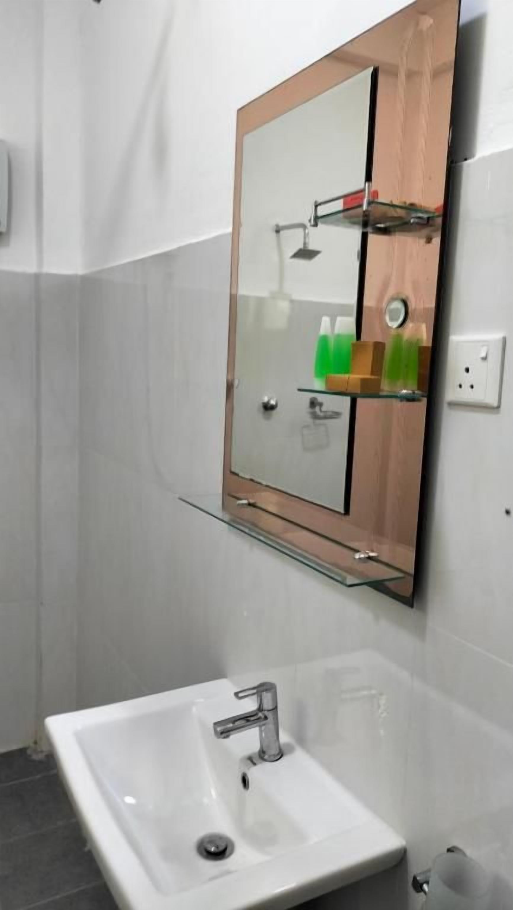 Un baño con un lavamanos blanco, un espejo con marco de madera y un estante de vidrio sobre el lavamanos.
