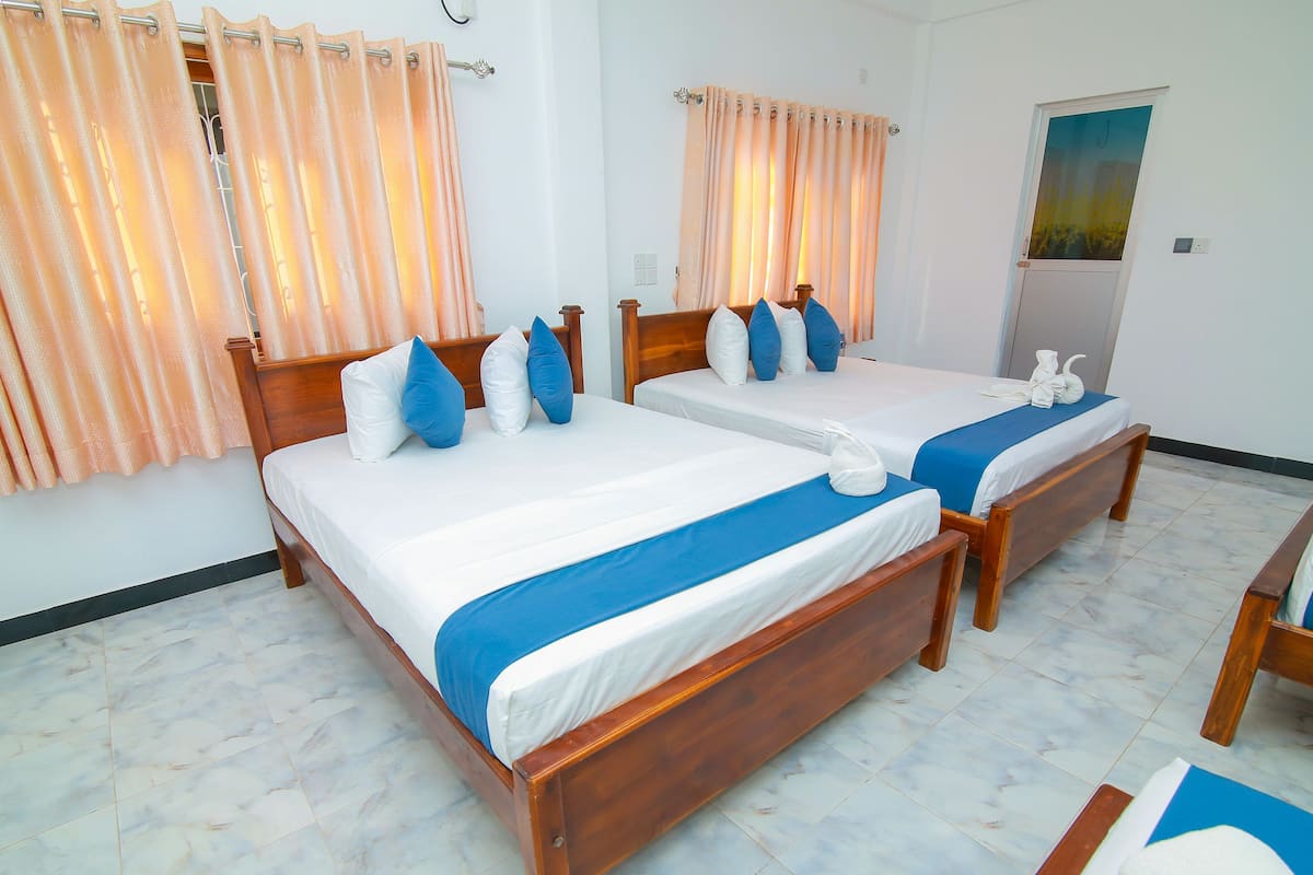 A hotel room with two wooden beds, white bedding, blue accents, and a view of the outdoors through a window.
