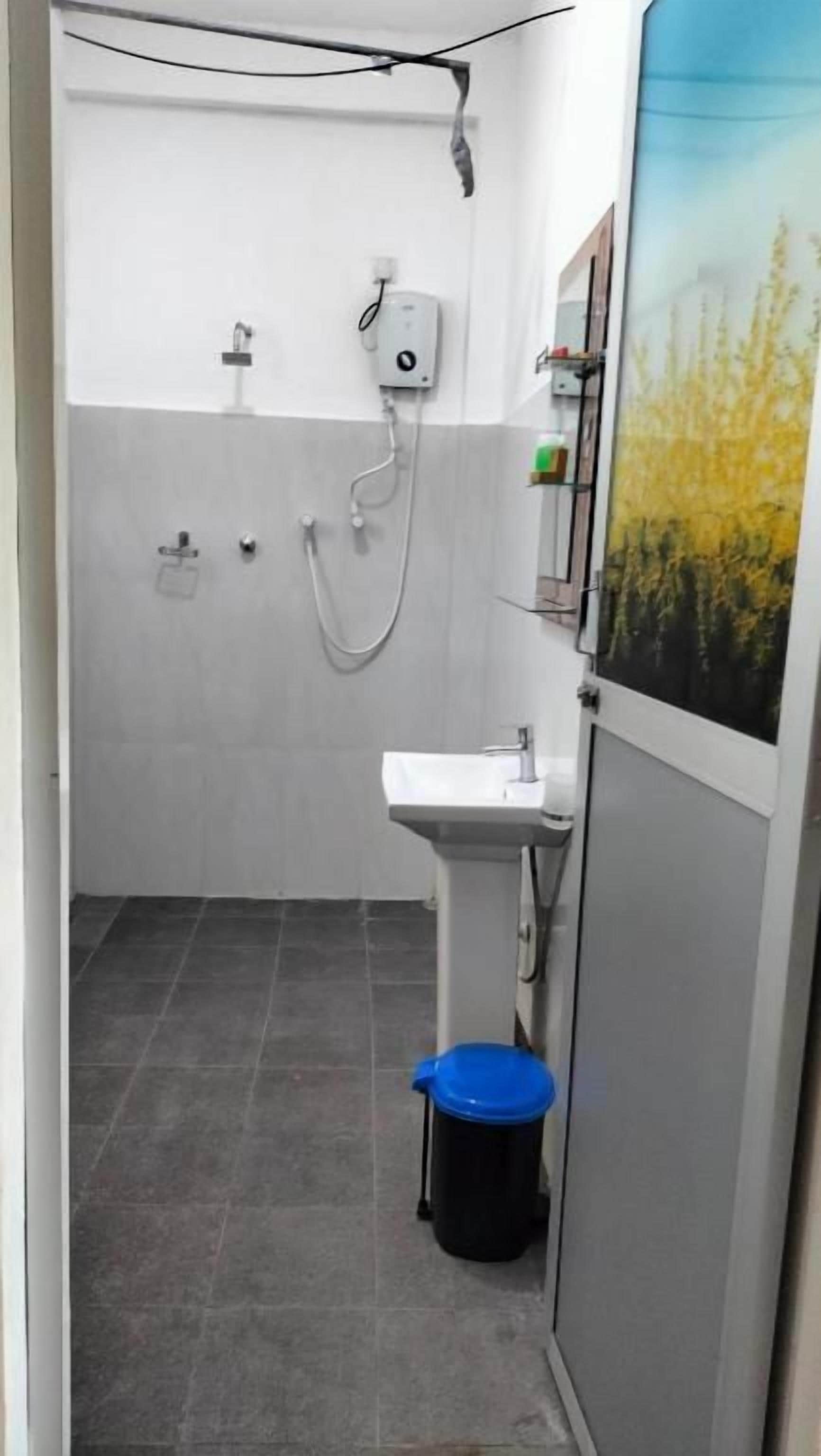 Un baño estrecho con un lavamanos blanco, una ducha y un bote de basura azul.