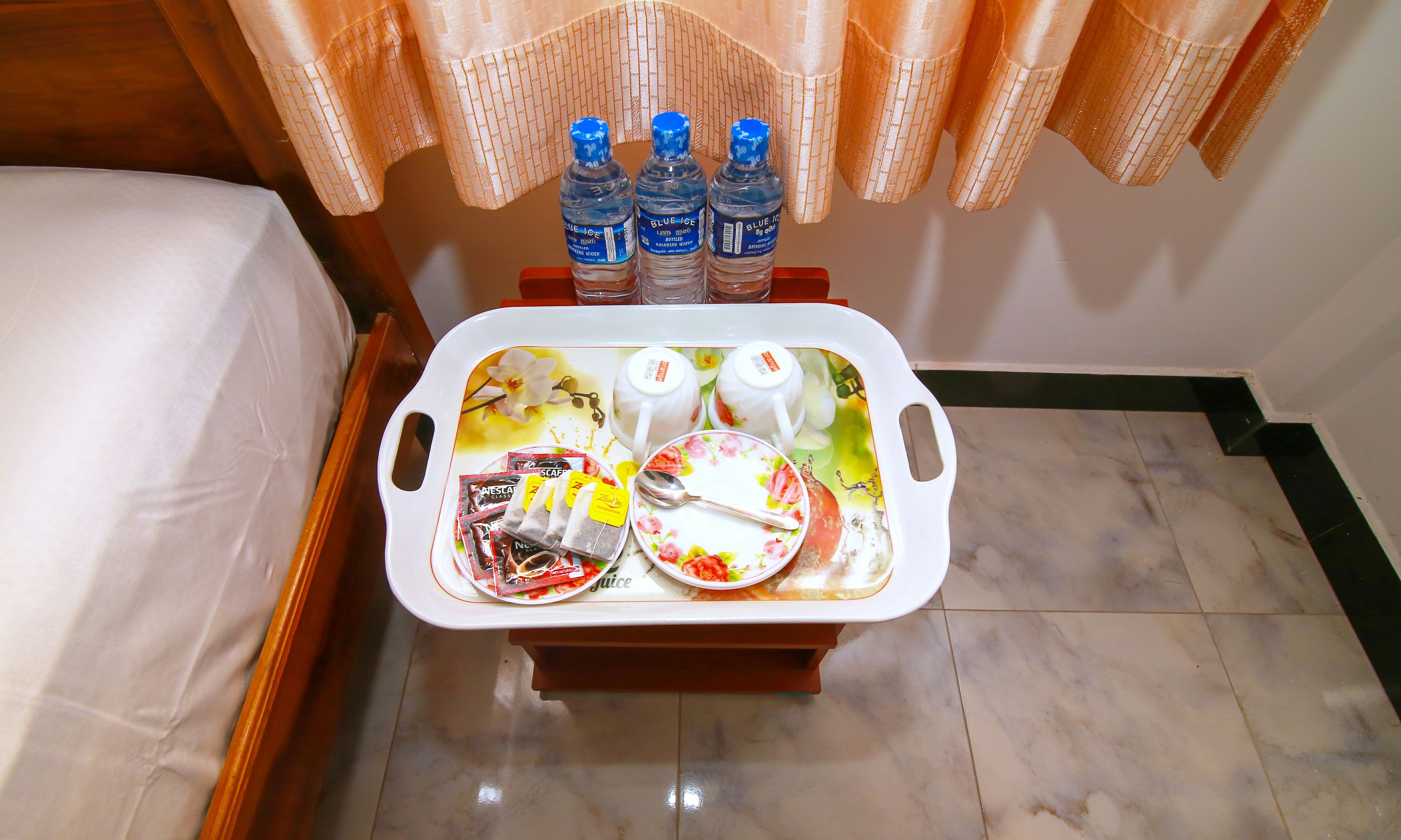 Une chambre d’hôtel avec une table de chevet sur laquelle se trouve un plateau avec une assiette, une cuillère et trois bouteilles d’eau.