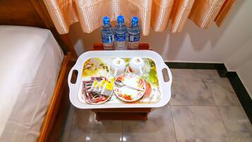 Une chambre d’hôtel avec une table de chevet sur laquelle se trouve un plateau avec une assiette, une cuillère et trois bouteilles d’eau.