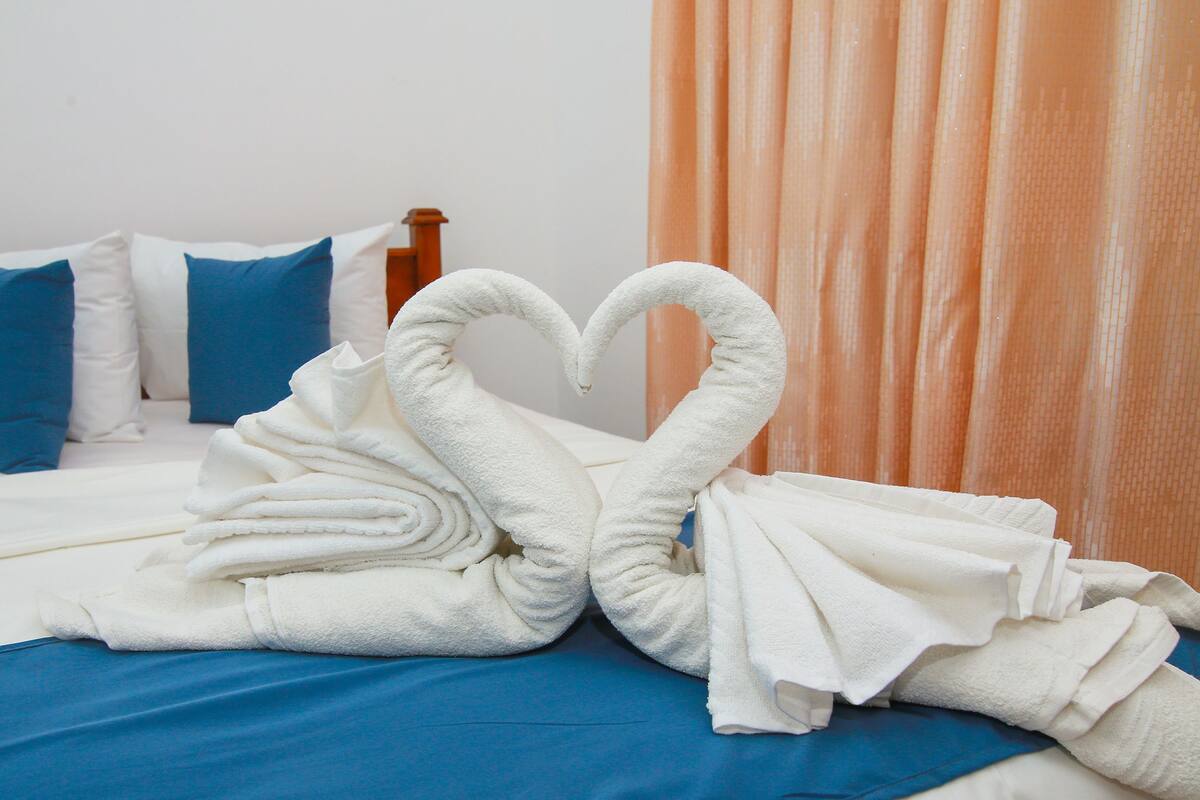 A bed with a heart-shaped towel arrangement, blue pillows, and a wooden headboard.