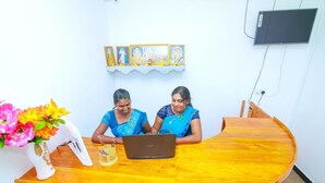 Two individuals seated at a wooden table with a laptop, a vase with flowers, and a wall-mounted television. - Hotel Sun Blue (Trincomalee)
