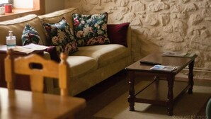 A living room with a sofa, floral cushions, a wooden coffee table, and a stone wall. - Hotel Eth Saueth (Naut Aran)
