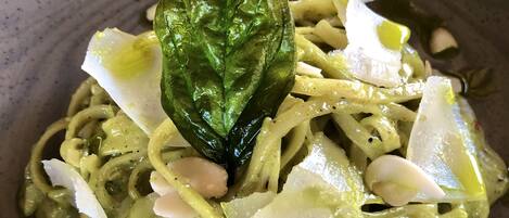 A bowl of pasta with a green sauce, garnished with a basil leaf and shaved cheese.