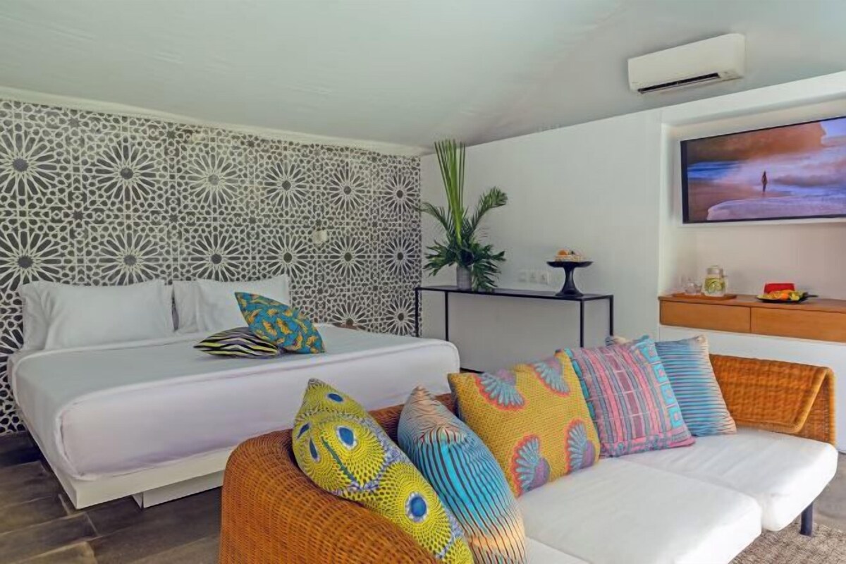 A bedroom with a bed, a sofa, a TV, and a decorative wall.
