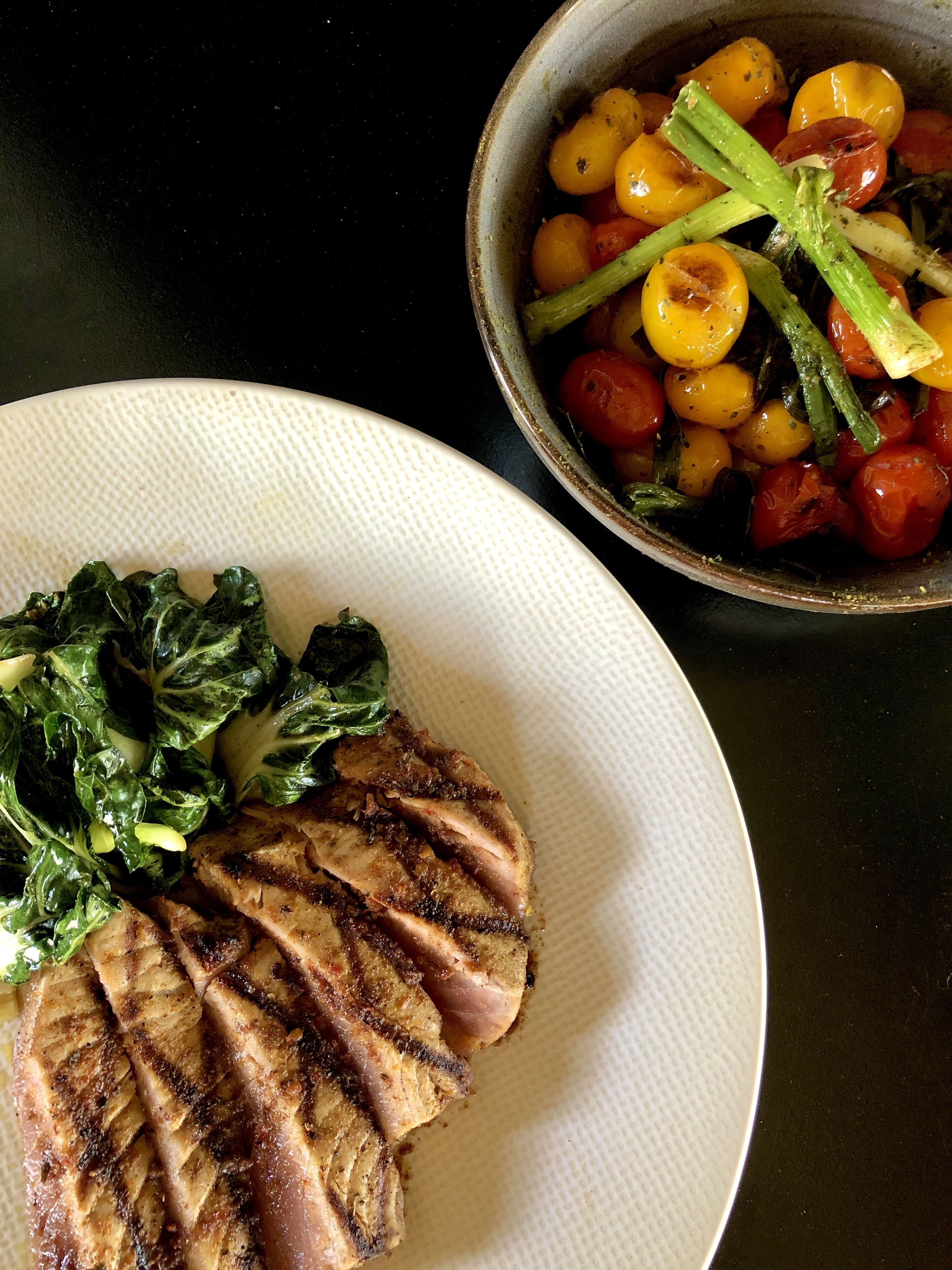 A plate with grilled meat and greens, and a bowl with roasted vegetables.