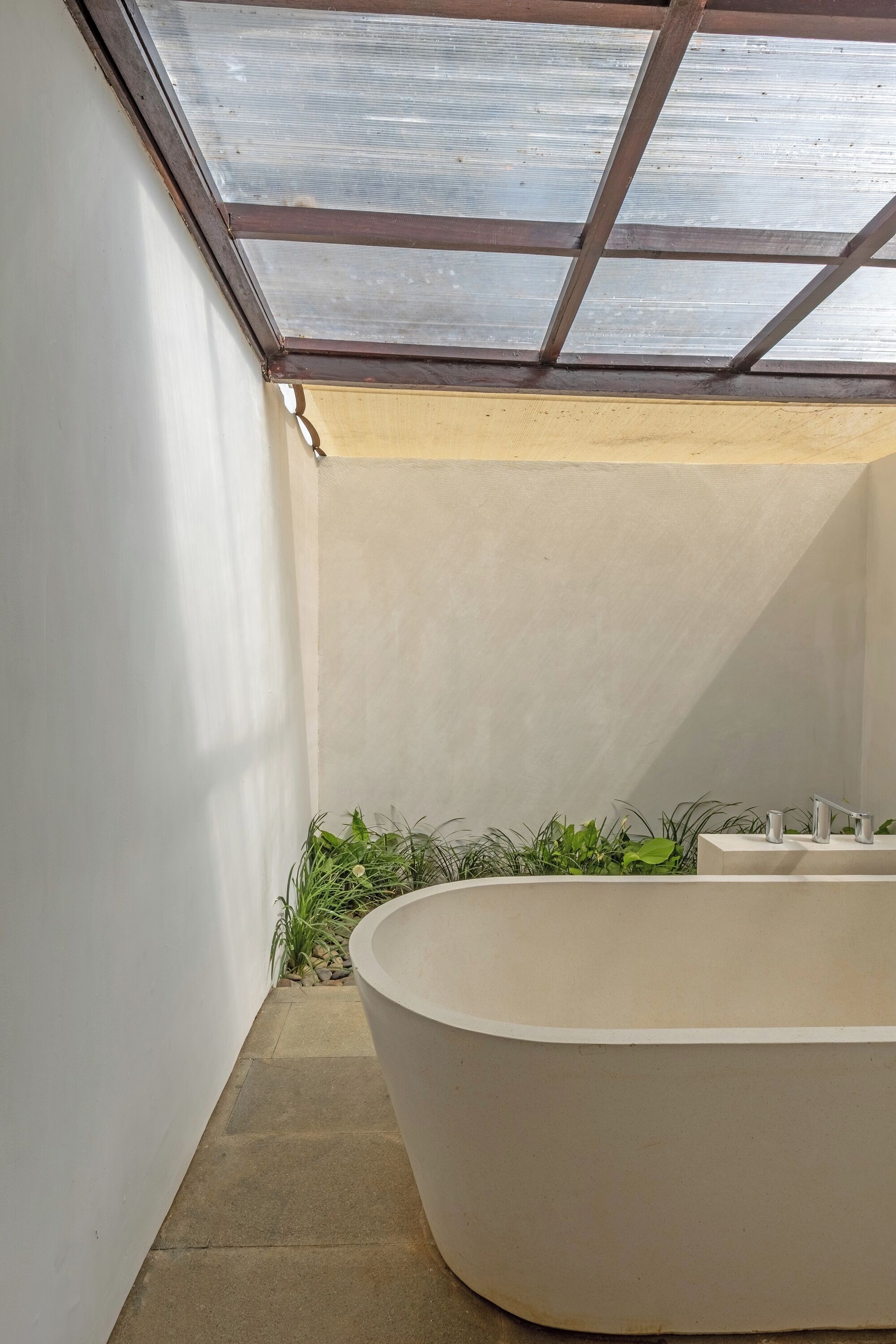 A modern bathroom with a freestanding bathtub, a skylight, and a small plant area.
