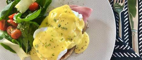 A plate with eggs benedict, spinach salad, and cherry tomatoes.