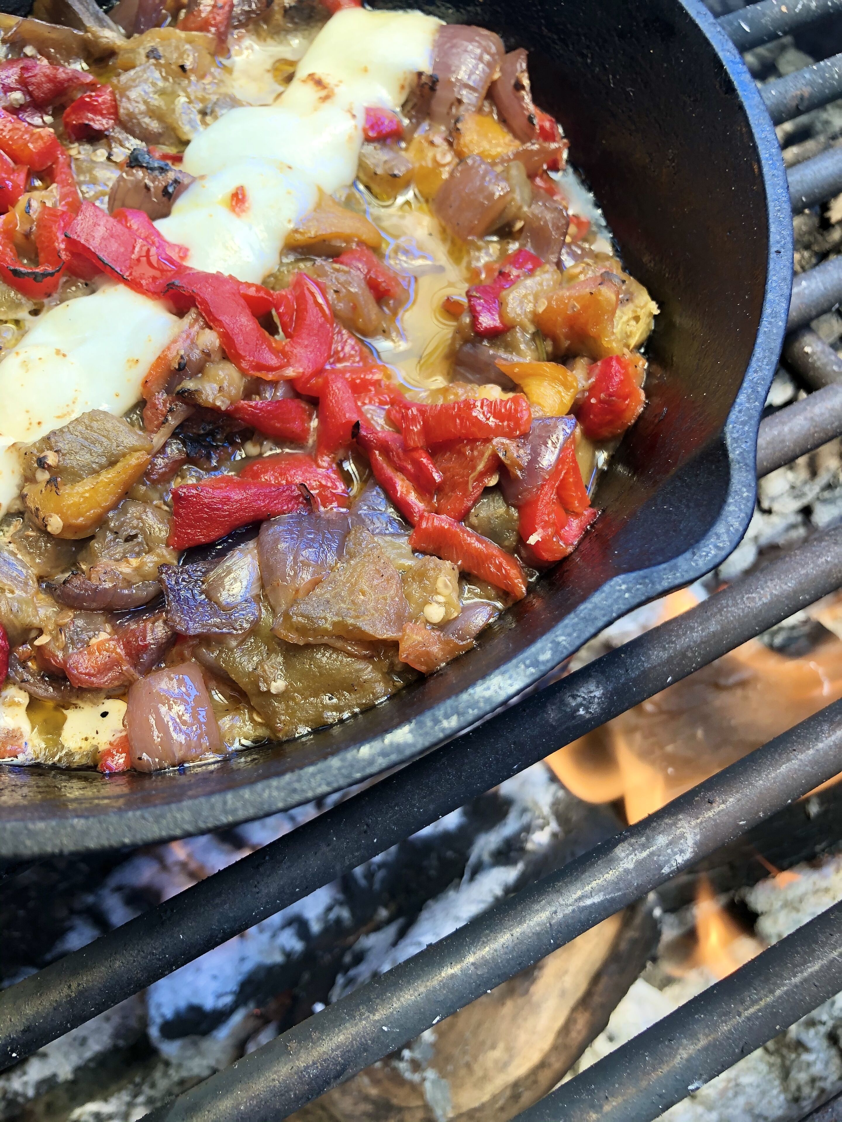 Ein gusseiserner Bratpfanne mit Essen, das über offenem Feuer zubereitet wird.