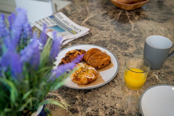 A breakfast setting with croissants, a glass of orange juice, and a newspaper on a marble countertop. - Shiloh (Carmarthen)