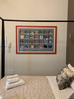 A hotel room with a bed, a wall-mounted artwork, a telephone, and a wall-mounted light fixture.
