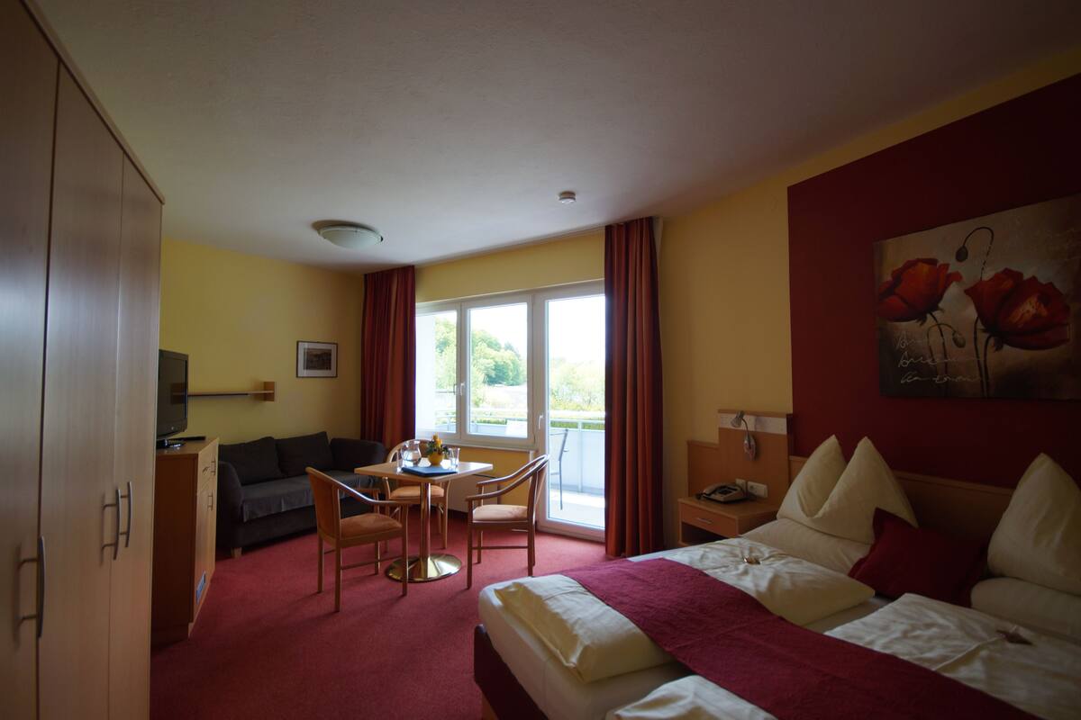 A hotel room with a bed, a desk, a chair, a sofa, and a window with curtains.