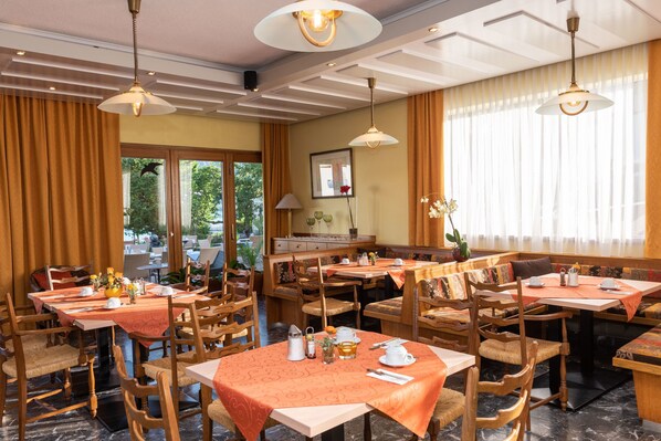 A restaurant with multiple tables and chairs, featuring a mix of wooden and cushioned seating. - Strandhotel Schabus (Velden am Wörther See)