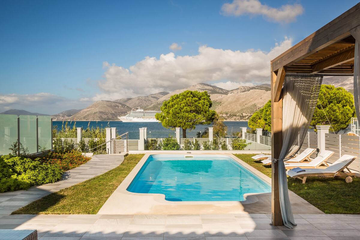 Una piscina rectangular con vista al mar y montañas al fondo.