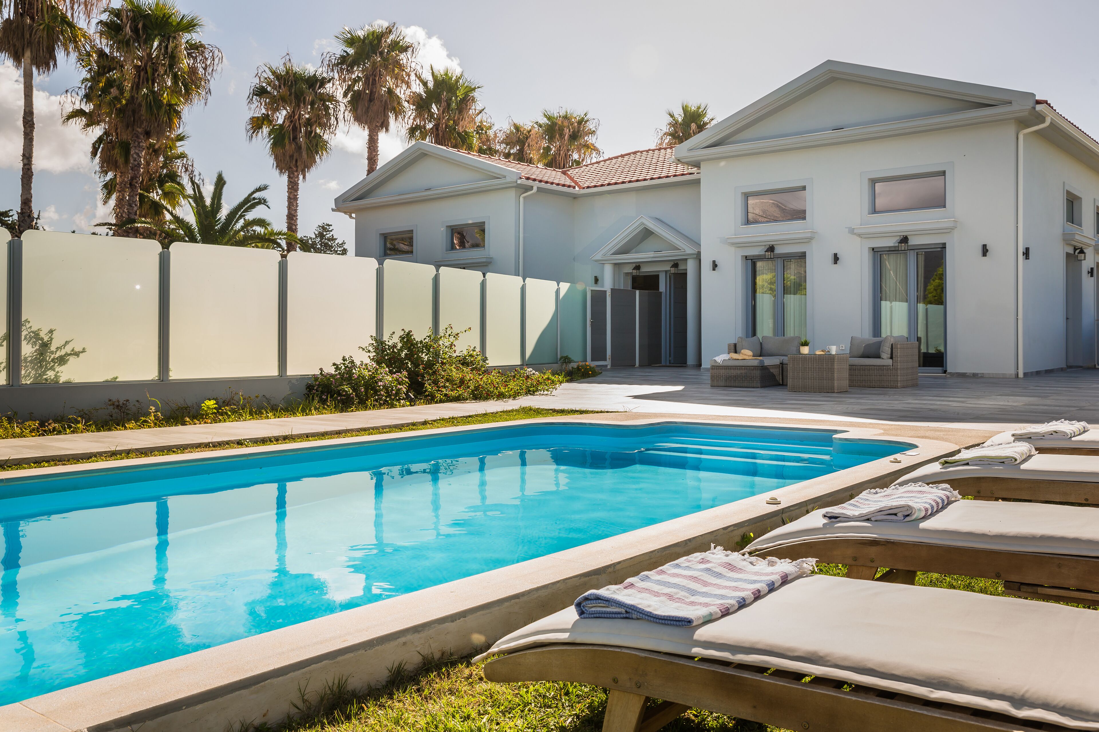 A swimming pool with lounge chairs, a patio area, and a building with a tiled roof.