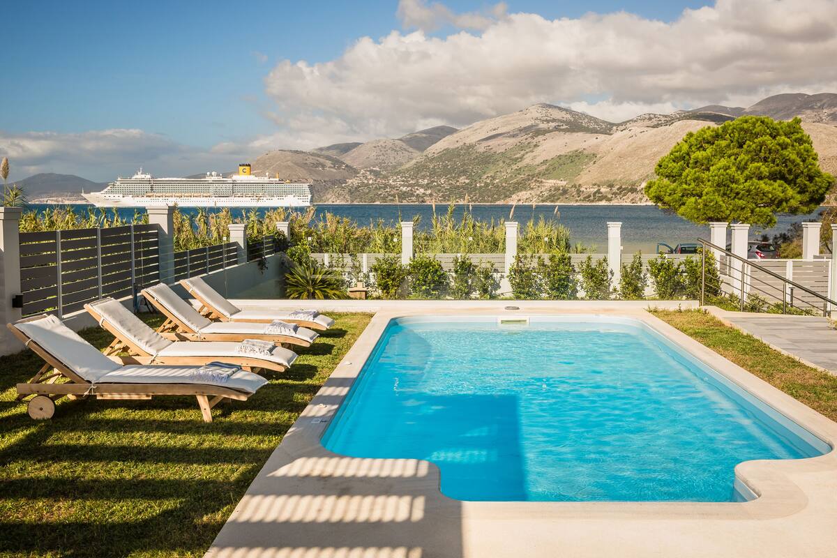 Una piscina con sillas de descanso, vista al mar y montañas al fondo.