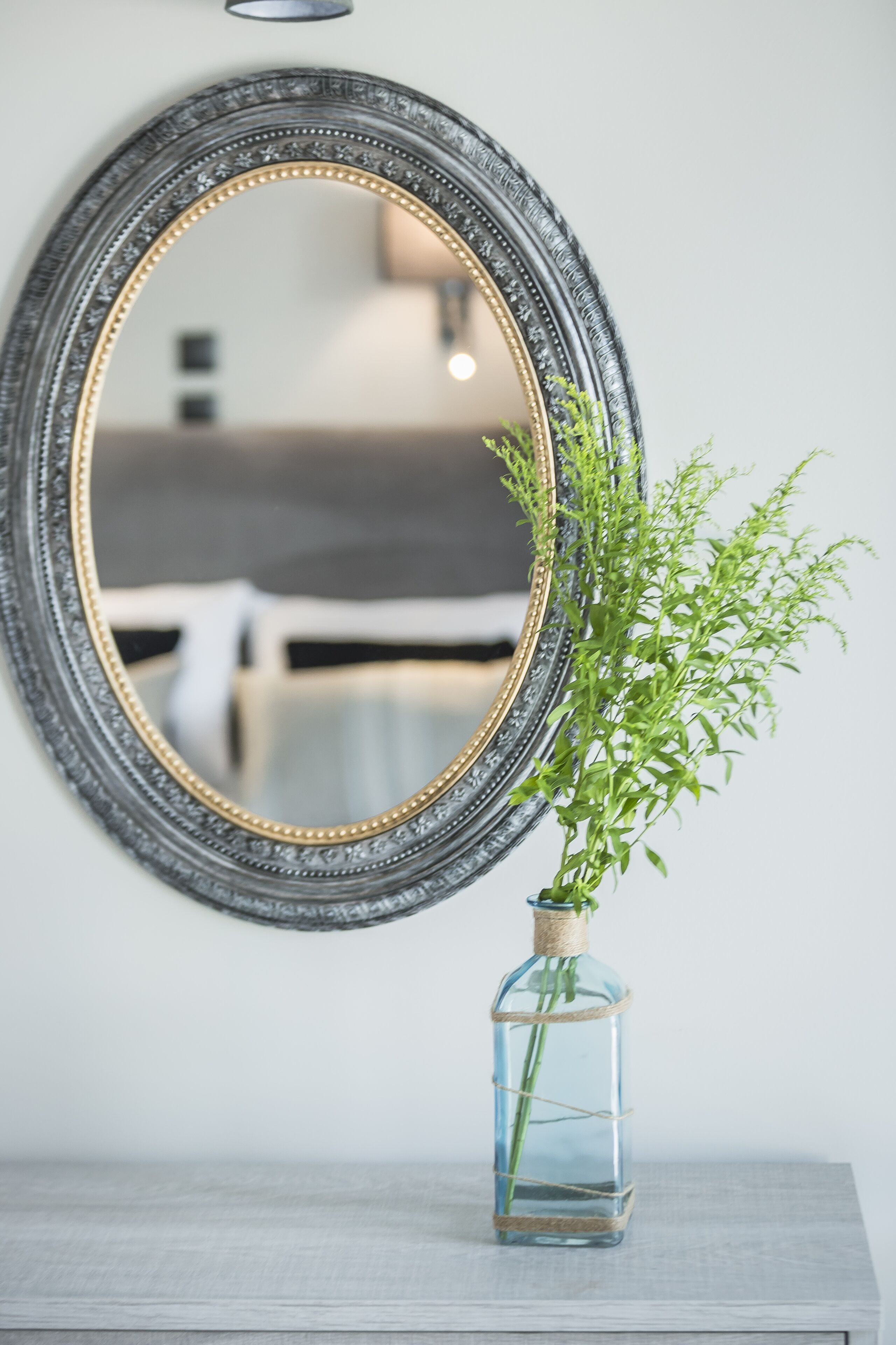 A mirror with a decorative frame, a small vase with a plant, and a wooden surface.