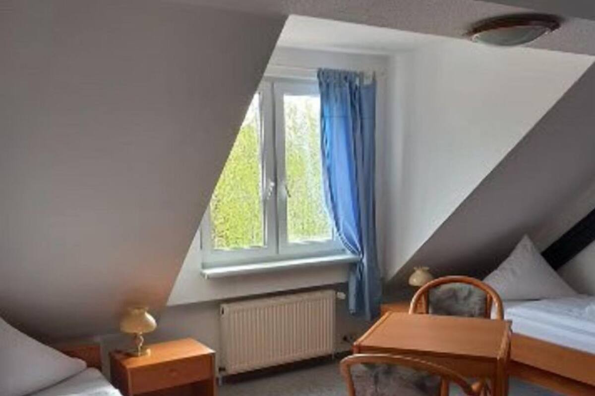 Un dormitorio ático pequeño y triangular con dos camas, una mesa y una silla.