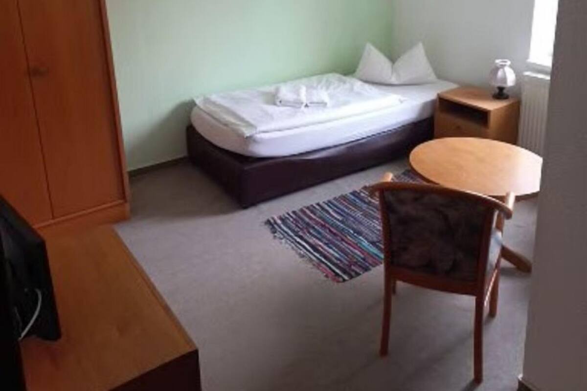 Un alojamiento pequeño y de una sola habitación con cama, un armario de madera, una mesita y una silla.