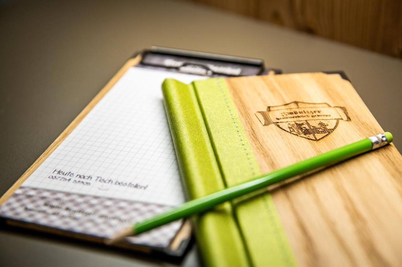 Um eskritório com um lápis verde sobre uma superfície de madeira, um caderno com linhas de grade e um logotipo.