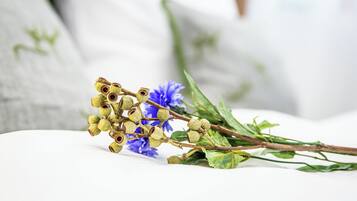 Una rama con flores secas y hojas verdes sobre una superficie blanca.
