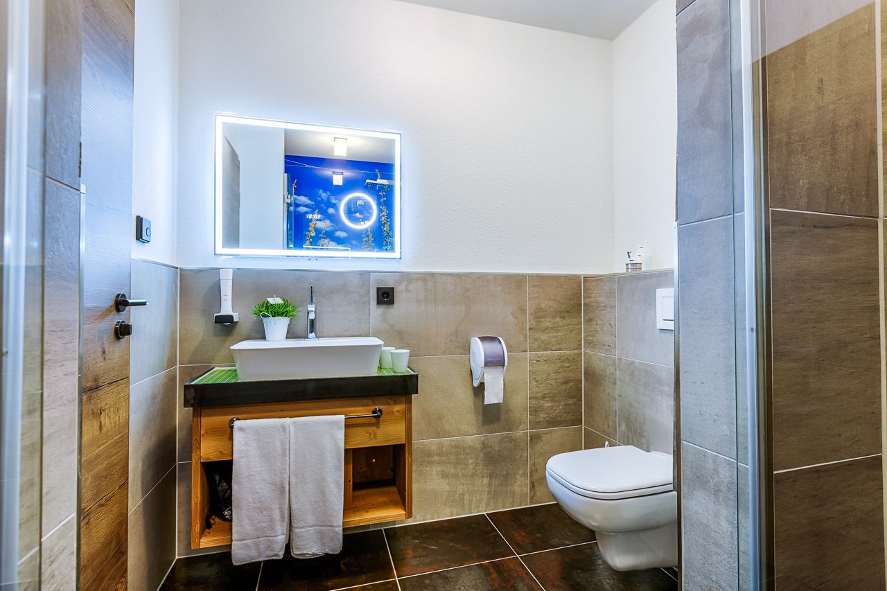 Un baño moderno con tocador de madera, un lavamanos, un espejo y un inodoro.