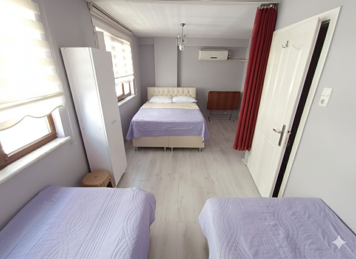 A bedroom with two beds, a window, a radiator, and a door.