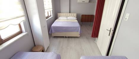 A bedroom with two beds, a window, a radiator, and a door.