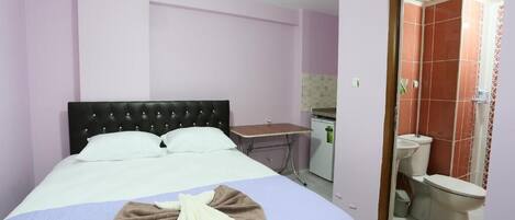 Un dormitorio con cama, escritorio y baño visible a través de una puerta abierta.