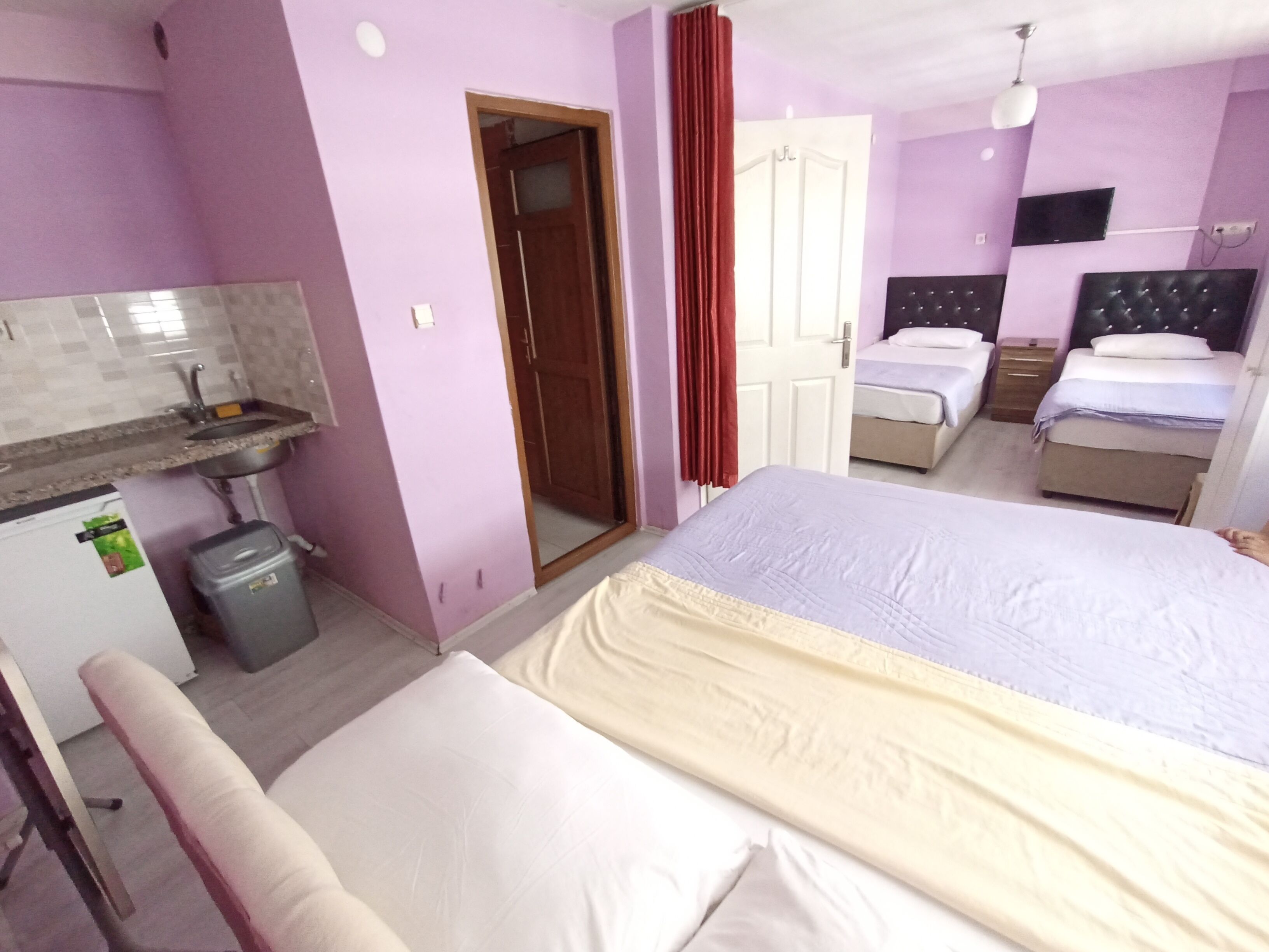 A hotel room with a bed, a small desk with a chair, a wardrobe, a bathroom with a sink, and a television mounted on the wall.
