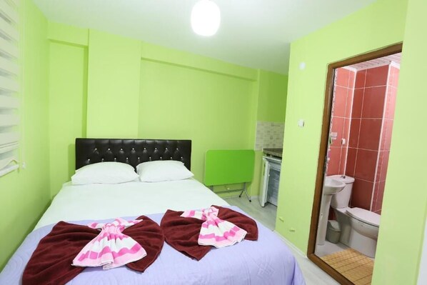 A room with a bed, a green wall, a bathroom with a red-tiled shower, and a white sink. - Yildiz Pansiyon (Amasra)