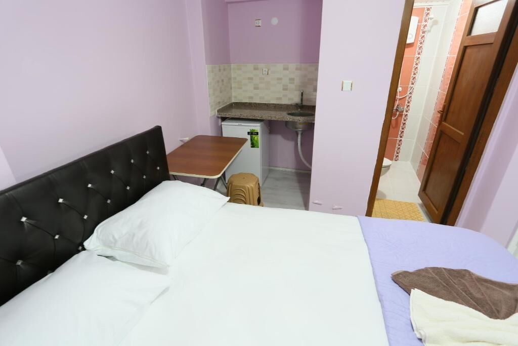 Una habitación pequeña y funcional con cama, una mesita y un rincón de cocina.