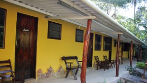 A yellow building with a wooden door labeled "Jupiter," a covered porch with wooden chairs, and a stone pathway. - Pousada do Sol (Alto Paraíso de Goiás)