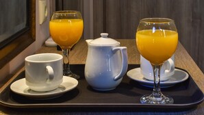 Una bandeja con una tetera blanca, dos tazas blancas y dos vasos de jugo de naranja.