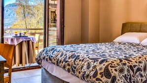 Un dormitorio con una cama, una mesa con dos vasos y una vista de la montaña a través de una ventana.