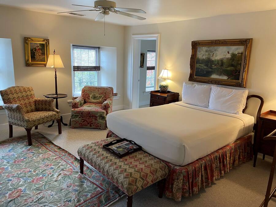 A spacious bedroom with a large bed, two armchairs, a small table, and a ceiling fan.