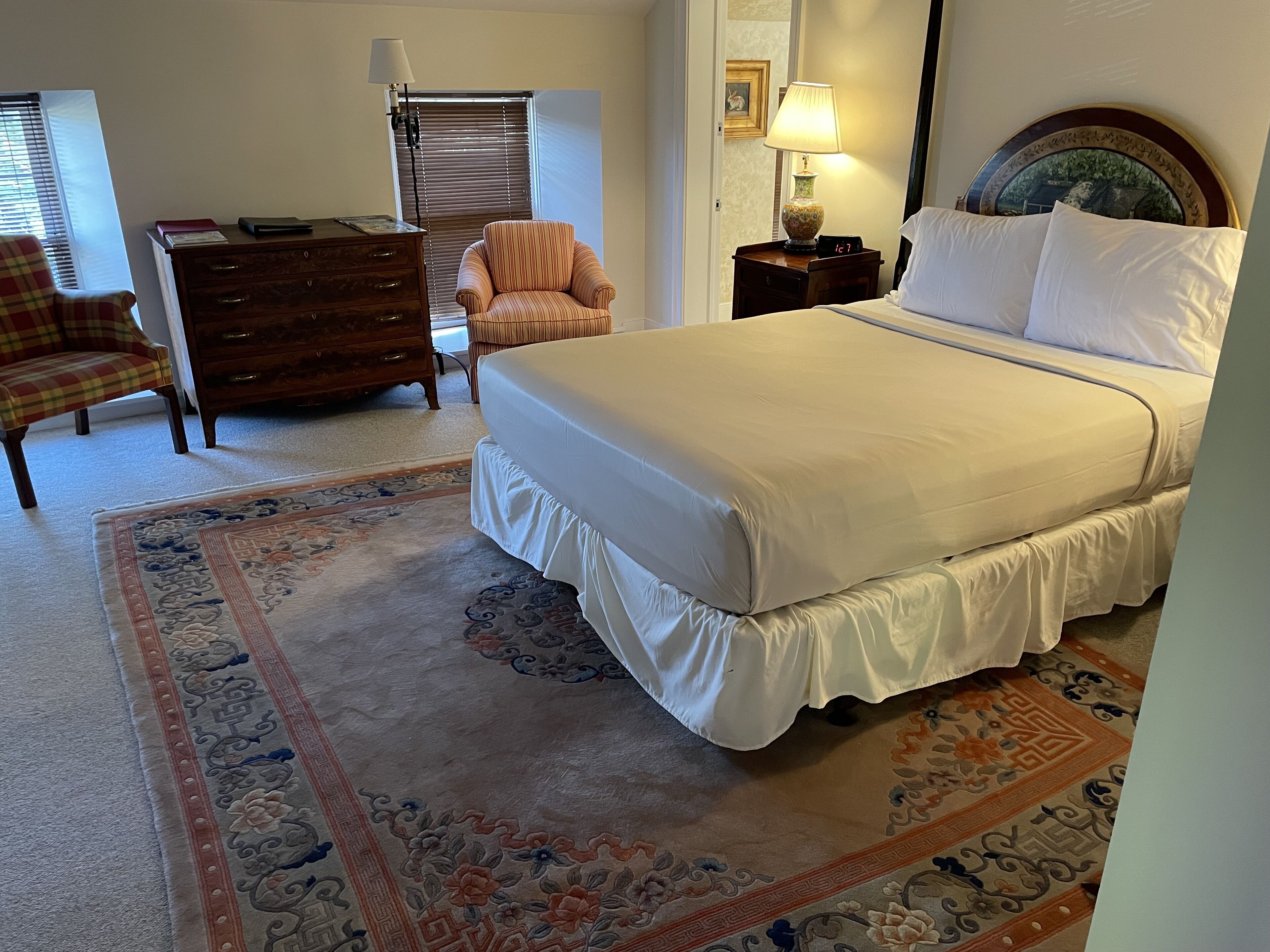 Ein Schlafzimmer mit einem großen Bett, einem Schminktisch, einem Sessel und einer Lampe.
