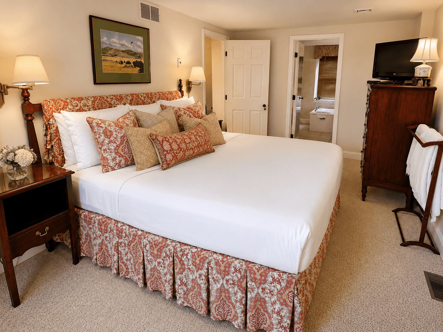 A hotel room with a large bed, two bedside tables with lamps, a television, and a bathroom visible through an open door.