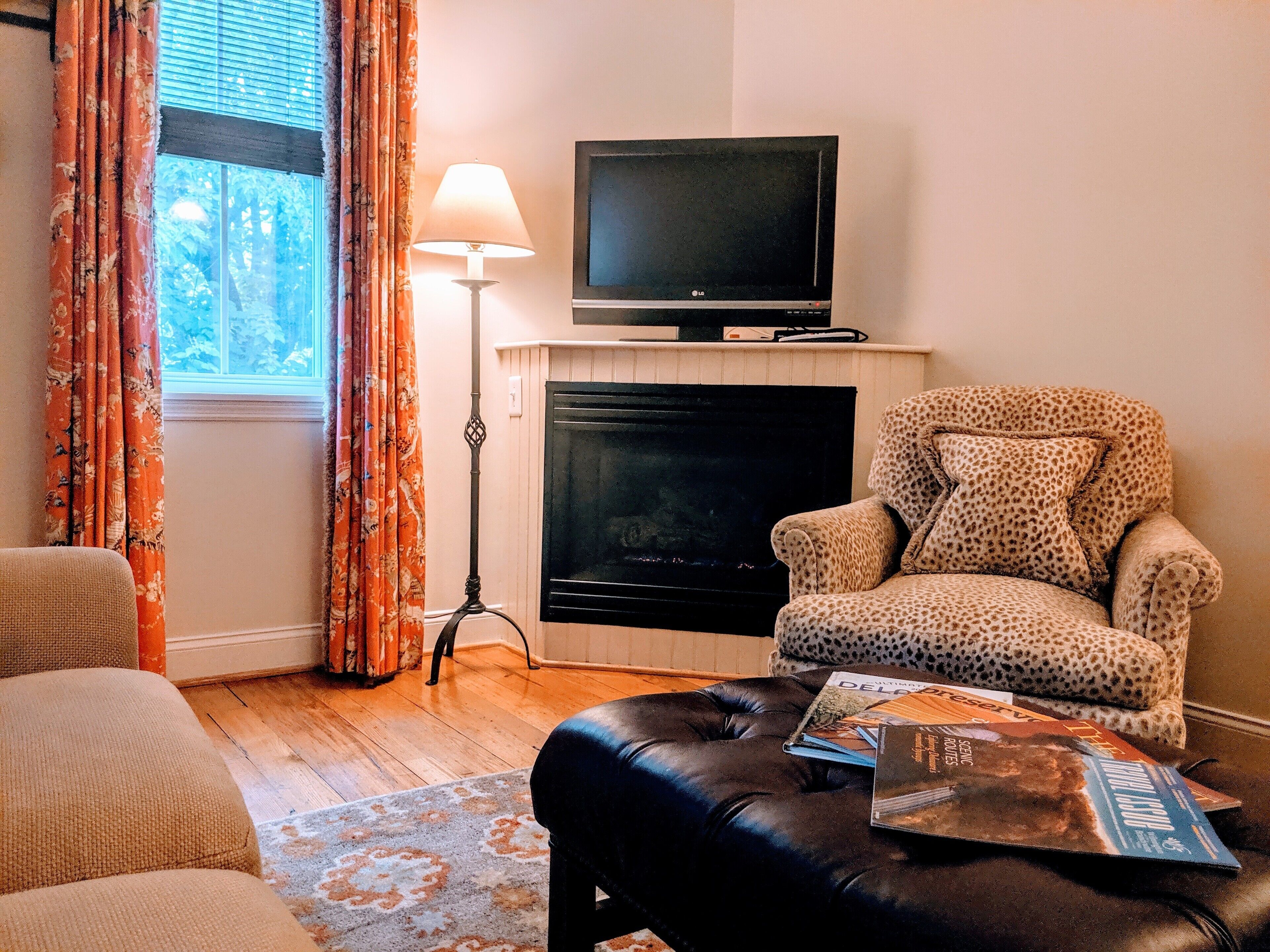 A living room with a fireplace, a leopard-print armchair, a sofa, and a coffee table with magazines.